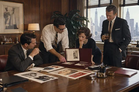 Four colleagues inspect advertising proofs in an open burgundy presentation case.