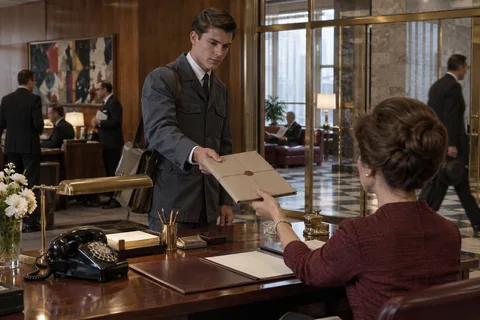A young courier passes a string-tied parcel across an office reception desk.