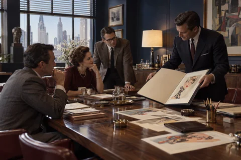 A presenter opens a large portfolio for three colleagues seated around a walnut table.