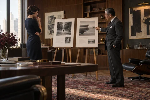 Two colleagues compare printed advertising layouts displayed on wooden easels.