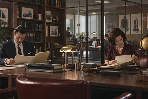 A man and woman independently examine folders at opposite sides of a library table.