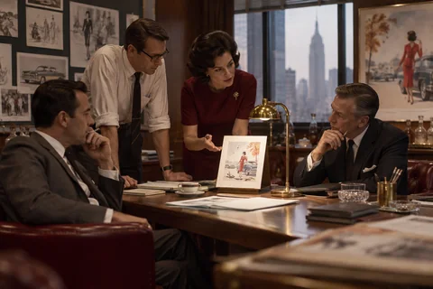 Four colleagues discuss an illustrated proof propped on a small brass stand.