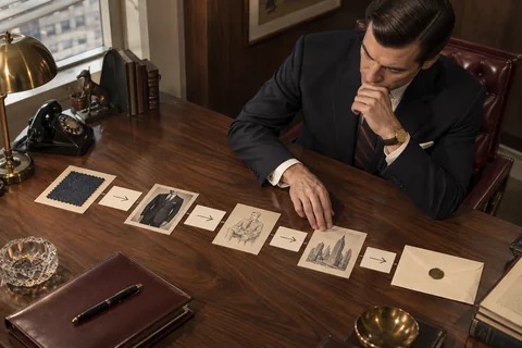 A strategist arranges photographs, arrow cards, a fabric sample, and an envelope across a walnut desk.