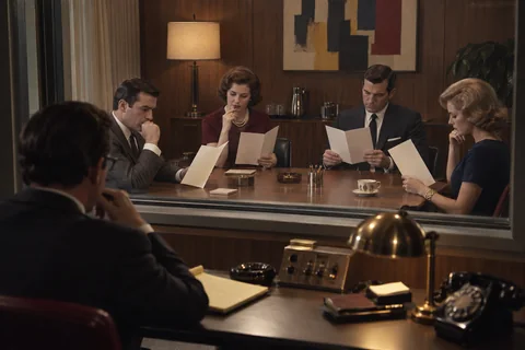 Four research participants study cream brochures while an observer watches through a glass partition.