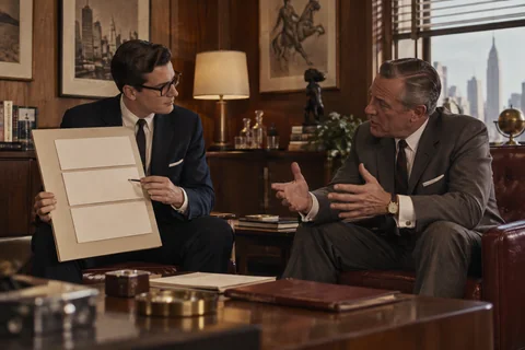 Two seated colleagues discuss three blank cream panels on a small presentation board.