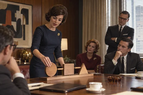 A woman demonstrates linked wooden shapes while four colleagues watch around a conference table.