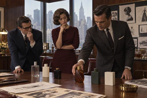 Three colleagues compare a row of unbranded sample bottles on a walnut presentation table.