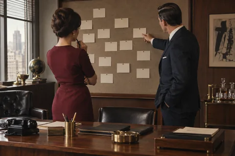 A woman and man examine blank cards pinned across a large fabric-covered board.